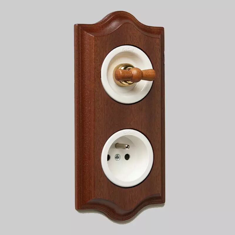 Sur un mur blanc, une plaque de finition en acajou de la collection Venezia accueille un interrupteur rotatif en porcelaine blanche avec manette en h�tre et une prise de courant en porcelaine blanche.