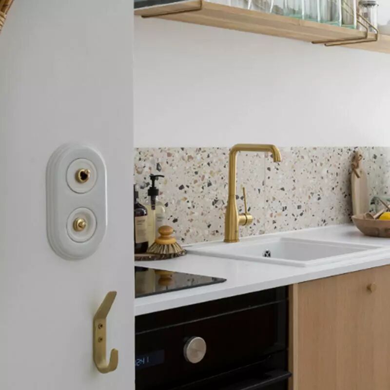 Dans une cuisine avec robinet en laiton et �quipements en bois se trouve une plaque de finition double en porcelaine blanche accueillant un interrupteur en porcelaine blanche et levier dor�. Un bouton poussoir se situe �galement sur cette plaque, sous l'interrupteur va-et-vient. 