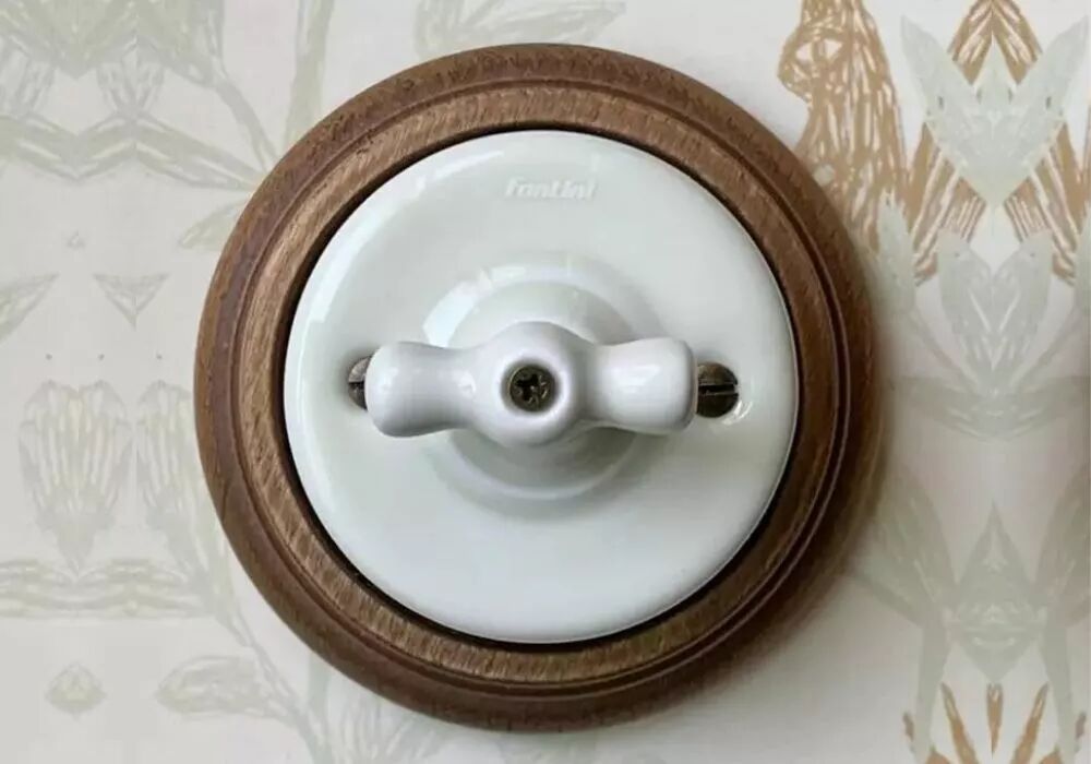 Installation, sur un mur tapiss�, d'un interrupteur en porcelaine blanche de la gamme Garby Colonial. Cet appareillage est plac� sur une plaque de finition en bois de h�tre vieilli.