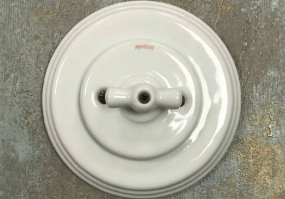 Sur un mur en b�ton, une plaque de finition simple en porcelaine blanche accueille un interrupteur � manette rotative blanche de la gamme Garby Colonial
