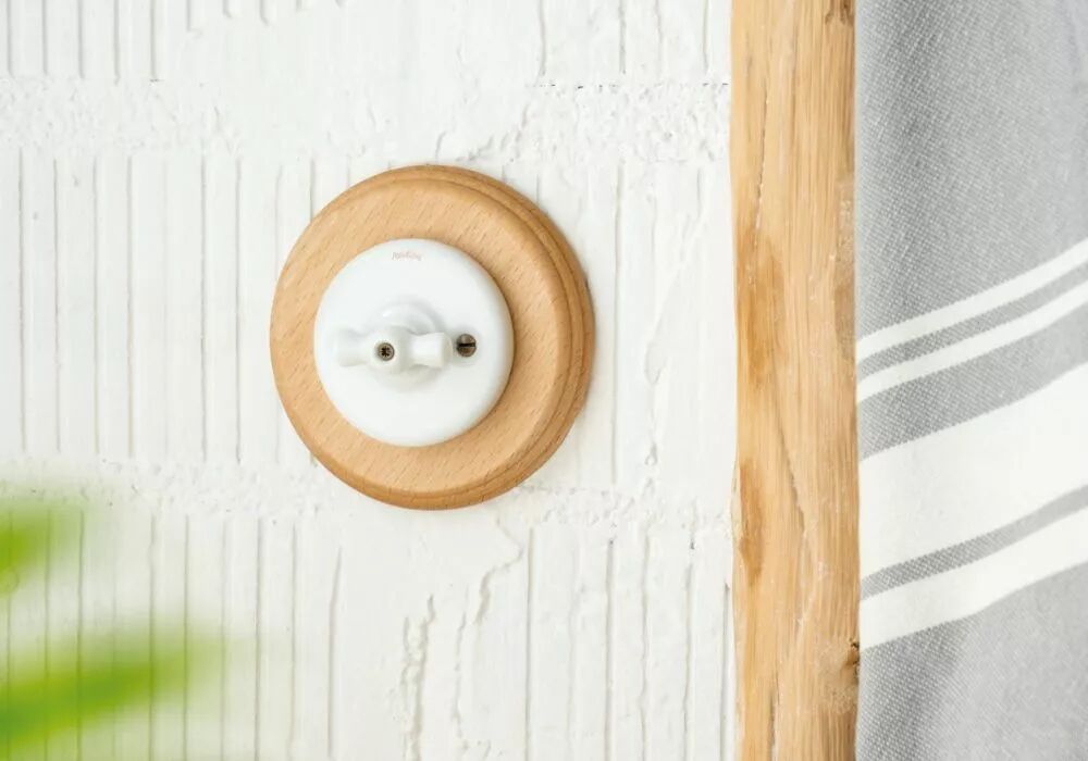 Sur un mur blanc l�g�rement stri�, une plaque simple en bois de h�tre accueille un interrupteur � manette rotative en porcelaine blanche.