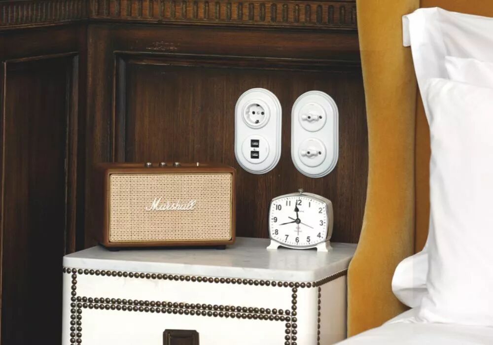 Plac�es au-dessus d'une table de chevet, � proximit� d'un lit, deux plaques de finition doubles verticales accueillent des appareillages. La premi�re accueille une prise de courant et une double prise USB. La seconde accueille deux interrupteurs � manette rotative en porcelaine.