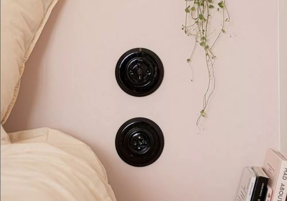 Deux plaques simples en porcelaine noire sont dispos�es l'une au-dessus de l'autre. Celle du haut accueille un interrupteur en porcelaine noire � manette rotative Garby Colonial. A gauche de ces appareillages, un lit peut �tre devin� gr�ce � l'oreiller et la couette qui entrent dans le cadre.