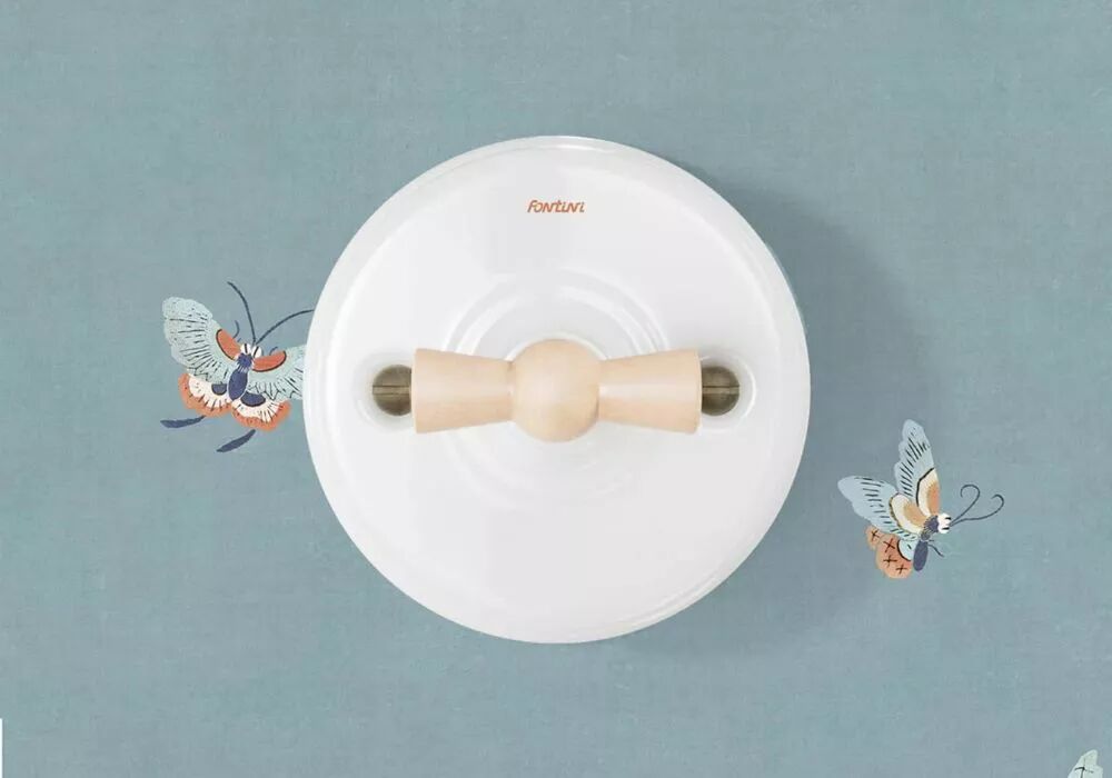 Sur une tapisserie bleue travers�e par deux papillons se d�gage la figure caract�ristique d'un interrupteur rotatif en porcelaine blanche. Il pr�sente une manette rotative beige en bois. 