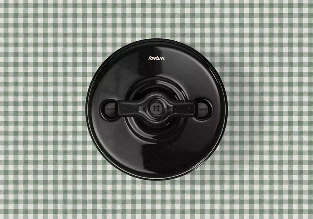 Sur un fond quadrill�, l'interrupteur en porcelaine noire � manette rotative distingue sa silhouette r�tro.