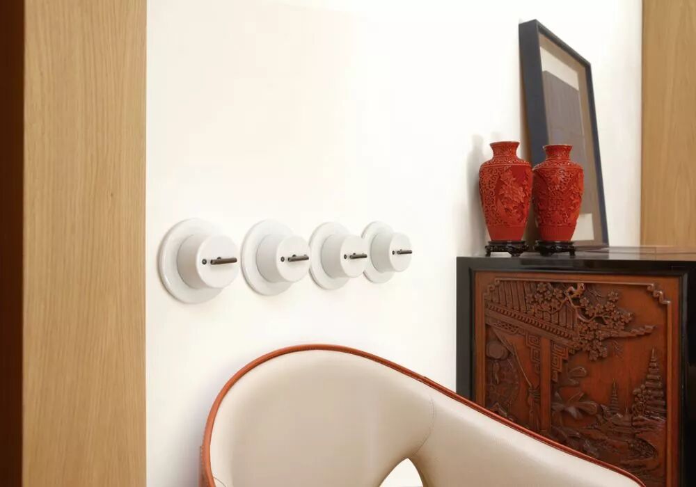 Au-dessus d'un fauteuil et � proximit� d'une commode travaill�e, se trouvent 4 interrupteurs � manettes en laiton vieilli sur des plaques simples en porcelaine blanche.