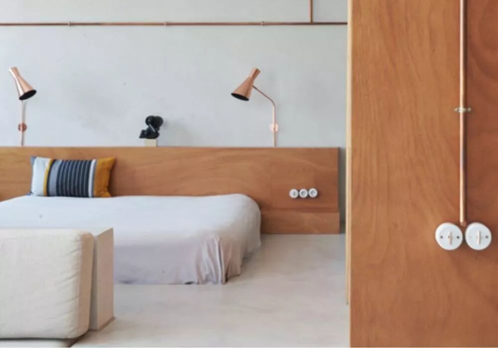 Dans une chambre en bois et un lit blanc, un conduit en cuivre descend le long du mur avec des interrupteurs en porcelaine avec leviers dor�s.