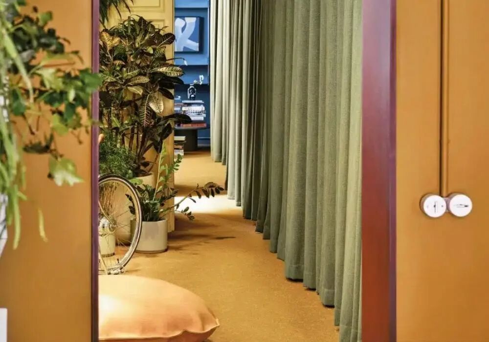  Dans une pi�ce avec mur jaune ouverte sur un couloir bord� par un rideau vert, nous pouvons observer deux interrupteurs en porcelaine blanche avec un conduit peint.